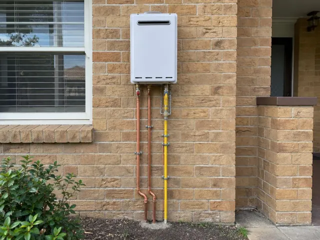 Wall-mounted hot water unit with copper and yellow pipework on a brick exterior wall in Enfield