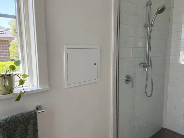Small access panel in a bathroom wall beside a tiled shower and window in Ashfield